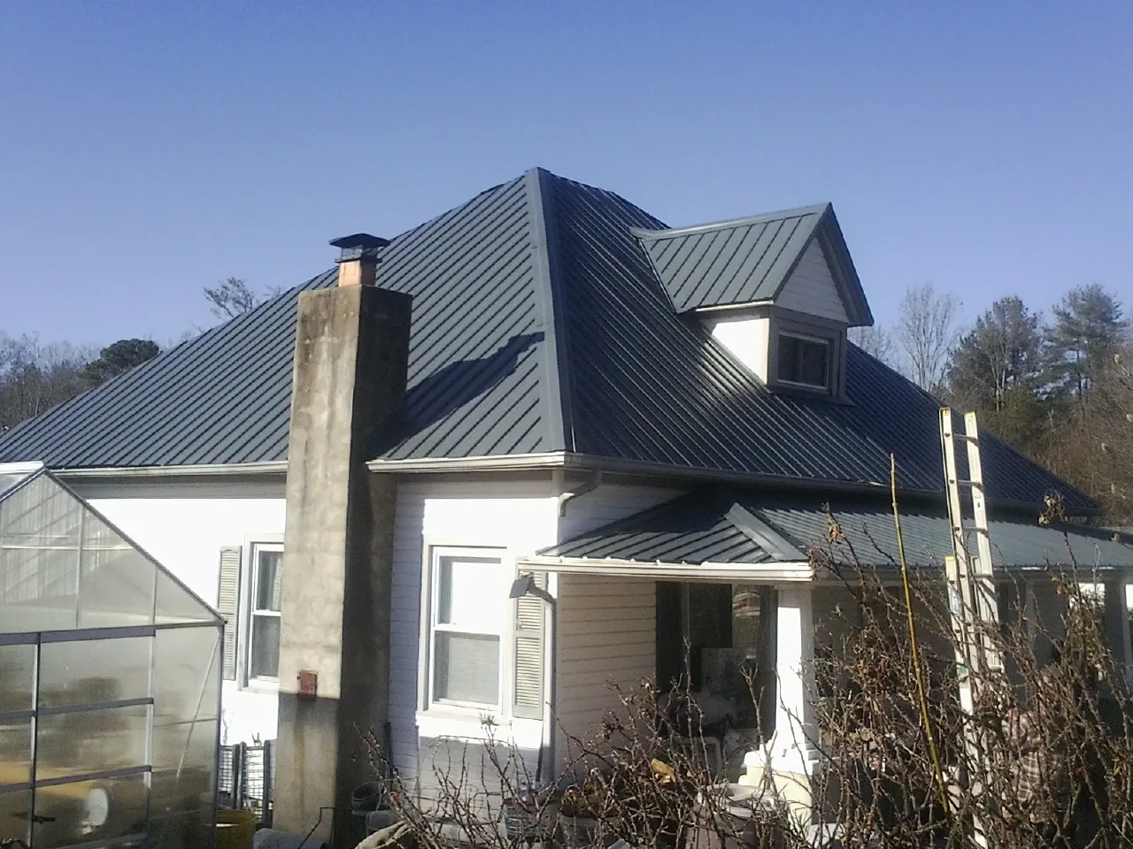 Dark blue standing seam metal roof on a white farmhouse with dormer — Slate & Tile Roof Repair by Roofing Brothers in Lathrop