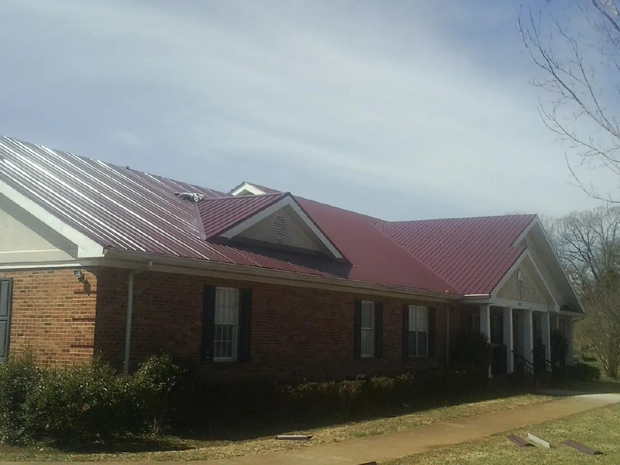 Red metal roof with gabled entries on a long brick building, from a Hail Damage Roof Repair job in Lathrop