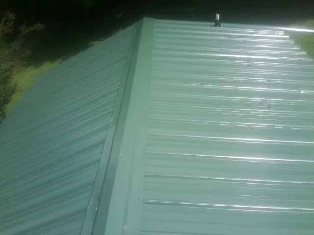 New green metal panels meeting at the ridge of a roof — Flat Roof Repair work by our crew in Lathrop