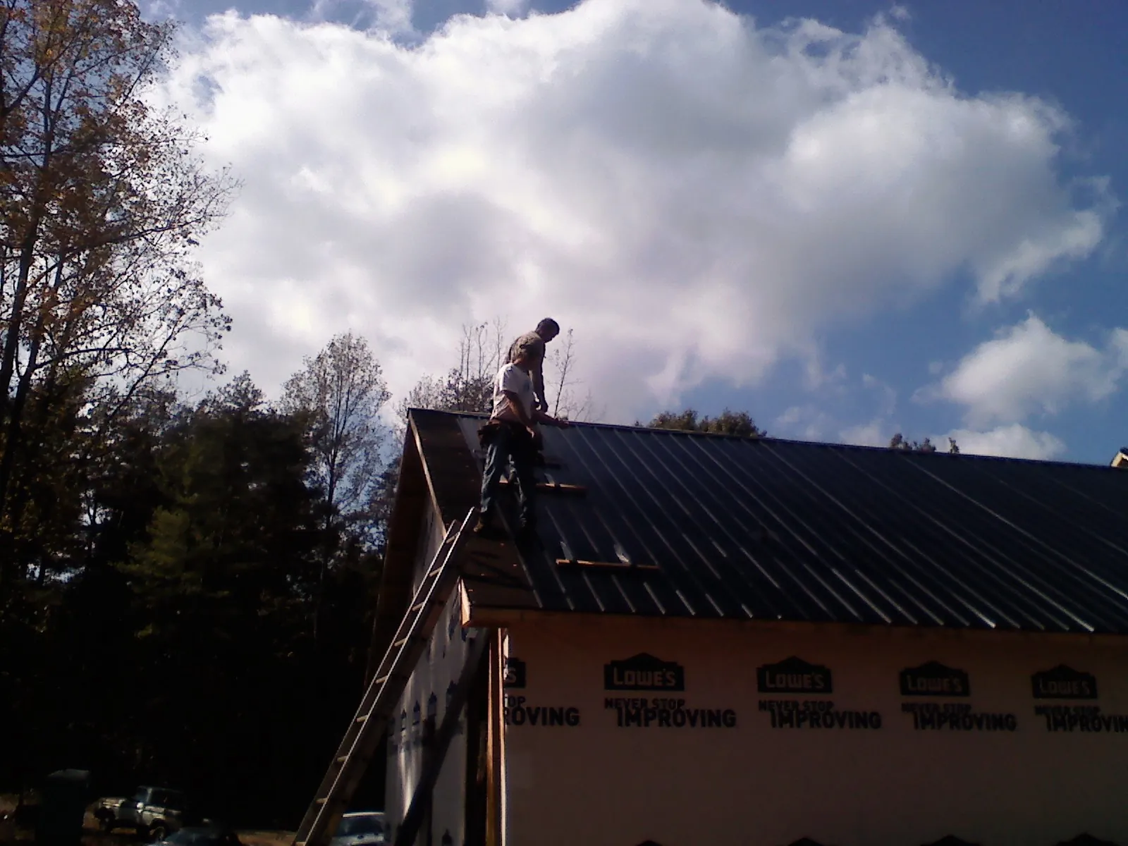 Roofer fastening dark metal panels high against a cloudy sky, from a Roof Inspection job in Lathrop